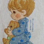 cross stitch charity quilt with baby boy in blue holding teddy bear