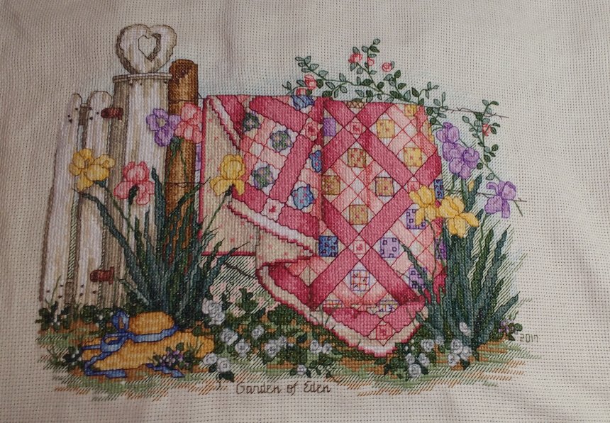cross stitch garden of eden payla vaughan quilt hanging on fencepost, bonnet, flowers